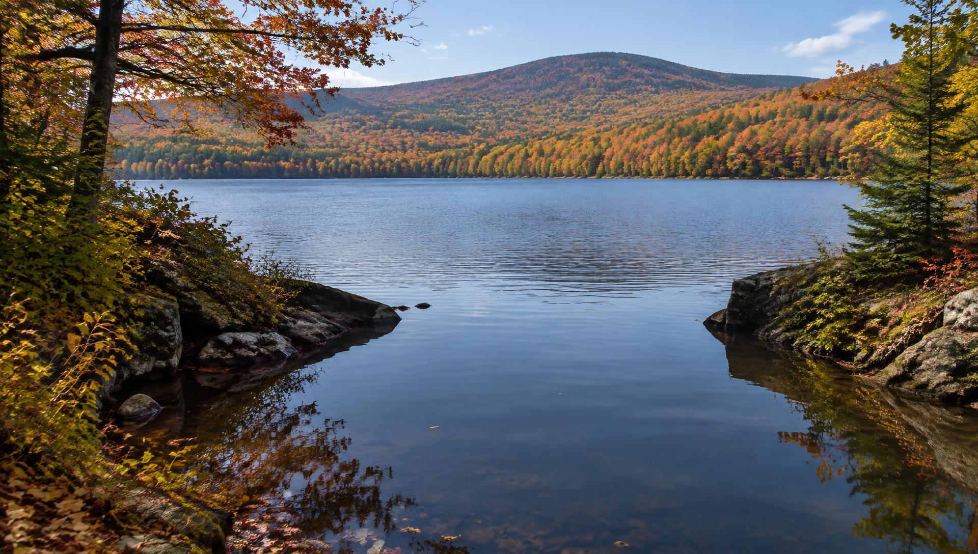 Wide wooded lake with a quiet cove in the foreground and autumn hardwoods along the far shore
